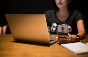 midsection-woman-using-smart-phone-laptop-table-darkroom-scaled